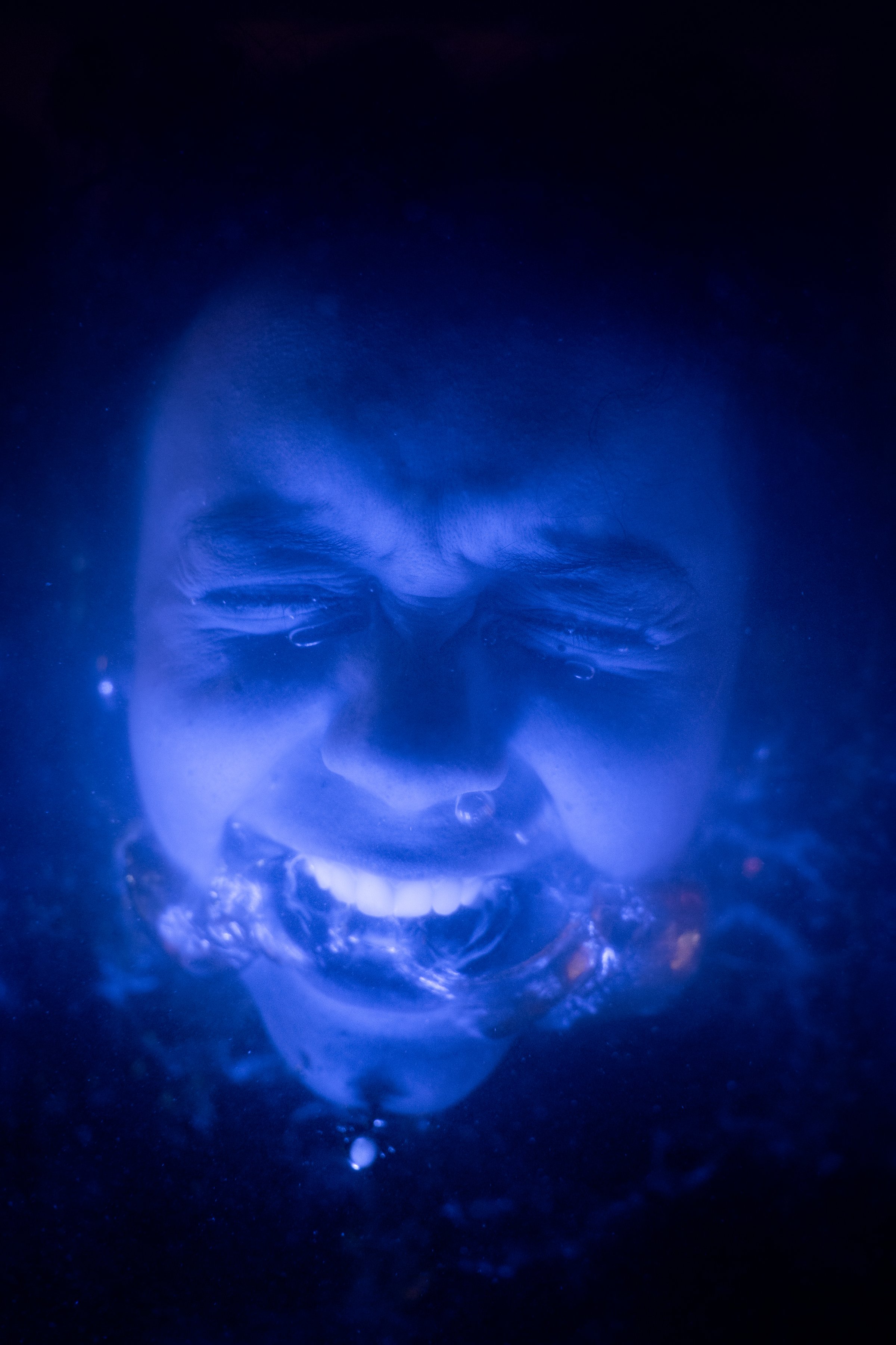 Face emerging from blue-lit water, dramatic underwater artistic portrait with glowing light
